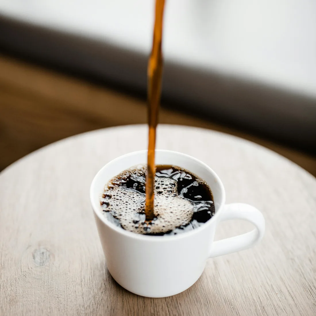 Kopi hitam dituang ke dalam cangkir putih di atas meja kayu